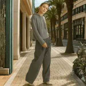 Woman in casual grey outfit posing on a sunny palm-lined street.