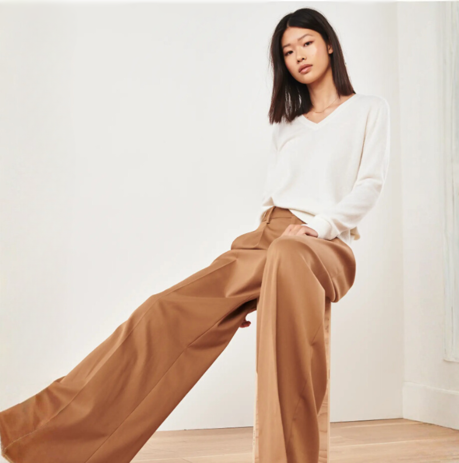 Woman in wide-legged brown pants and white sweater posing indoors.