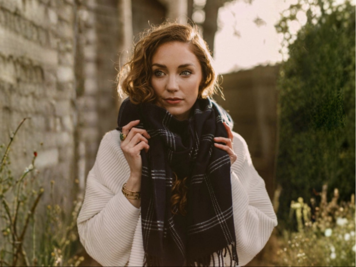 Woman wearing an ivory knit sweater layered with a dark plaid scarf