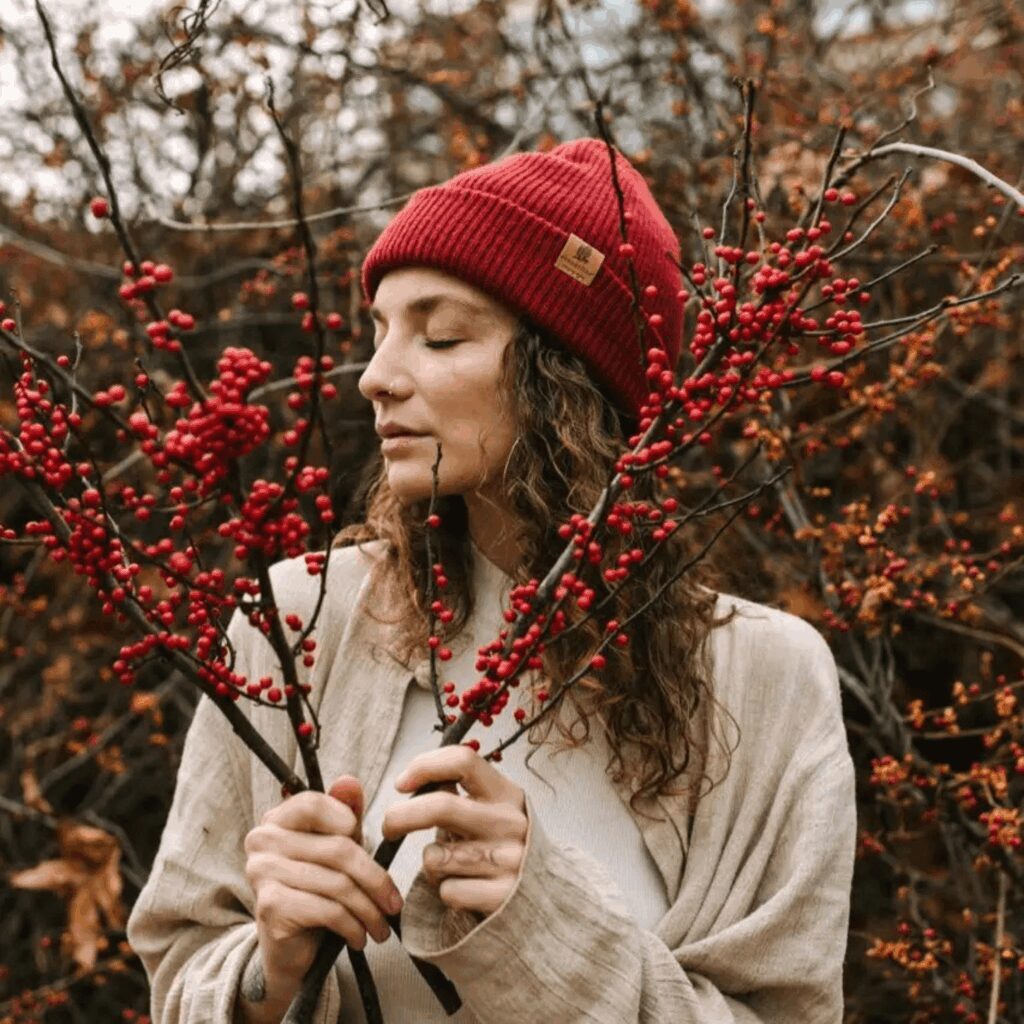 A woman in a red beanie holding red berries in a natural setting.