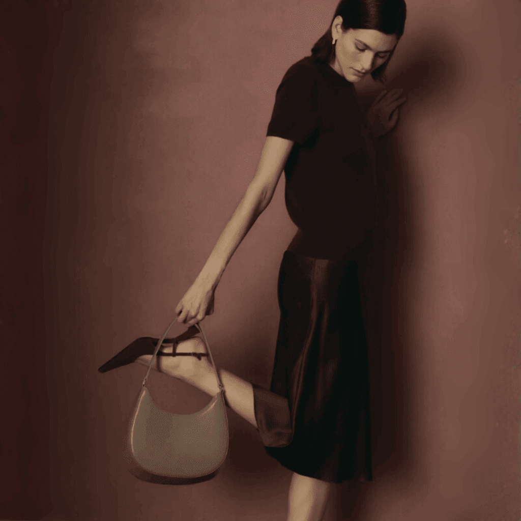 Pregnant woman in a dark dress holding a handbag against a brown background.
